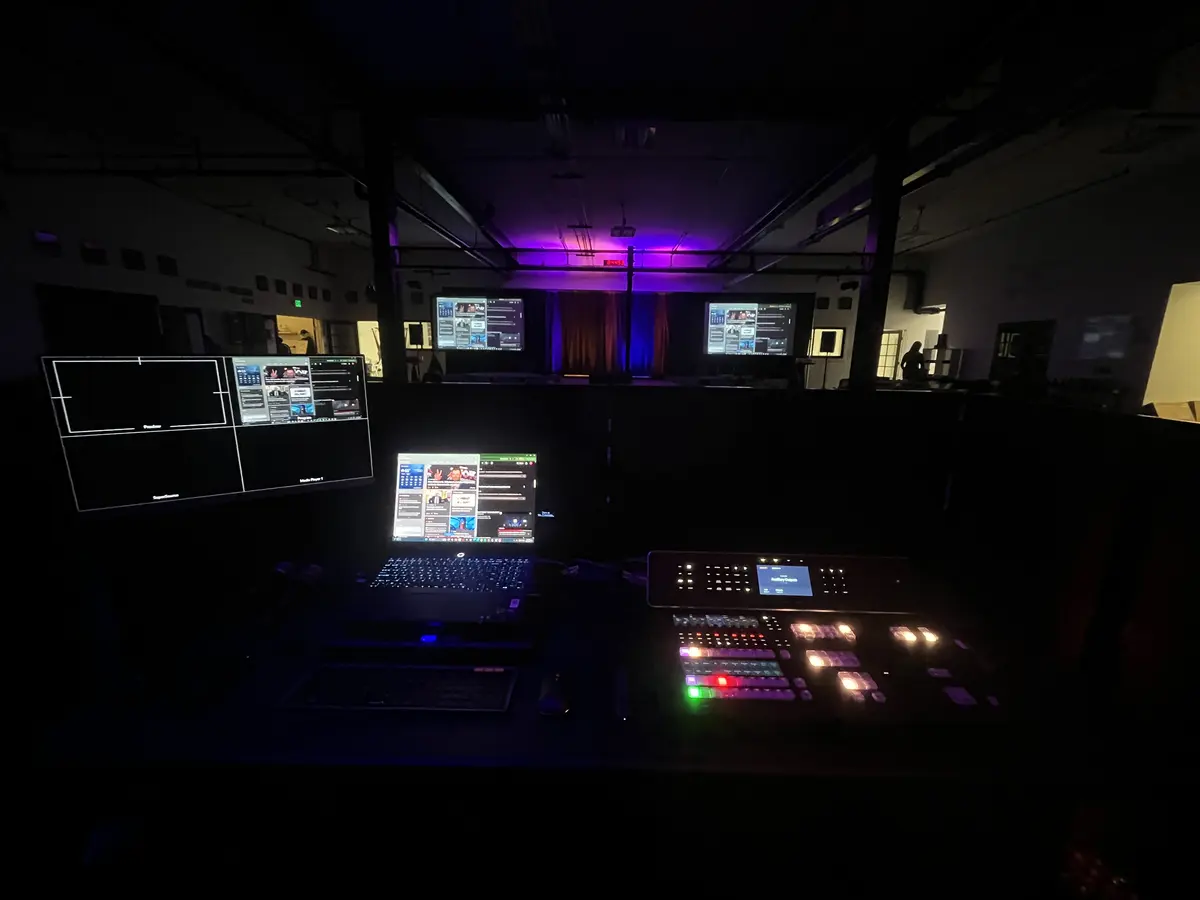 Windows laptop running a live video production setup next to a multiview monitor and video switcher